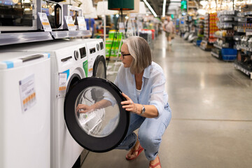 Middle-aged woman explores appliances while shopping in a large retail store showcasing home goods...