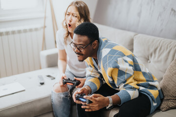 Two friends enjoy playing video games while sitting on a comfortable couch in a relaxed home...