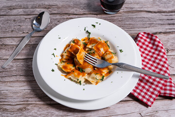 Fork lifting ravioli with tomato sauce from white plate