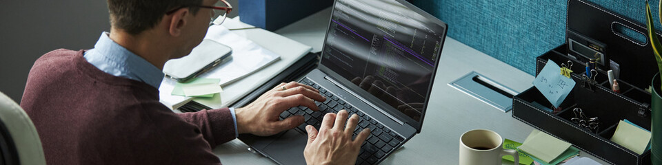 Header of Caucasian young man working on laptop at desk, typing programming code on computer in...