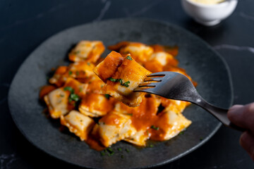 Ravioli pasta with tomato sauce and parsley topping on elegant dark grey plate