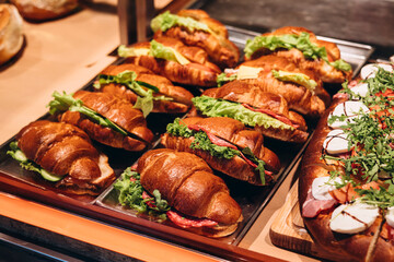Croissants with salami and greens on bakery display, close-up.