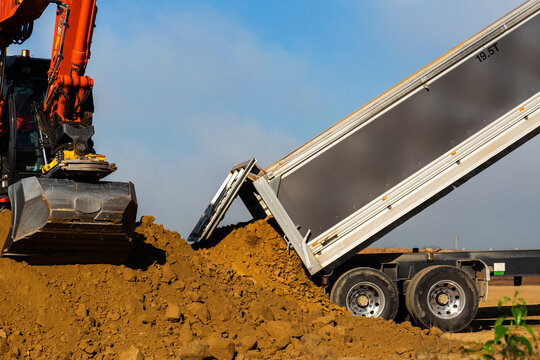Excavator earthmoving equipment working at construction site beside truck dumping dirt - Powered by Adobe
