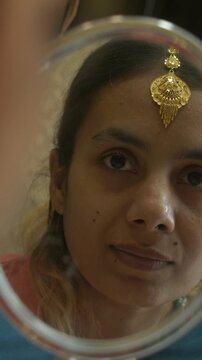 Young and beautiful south asian woman wearing gold jewellery while looking at mirror, Closeup, Vertical shot