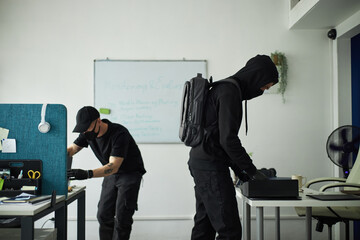 Two young male spies wearing black clothing and gloves, searching through office desks and drawers,...
