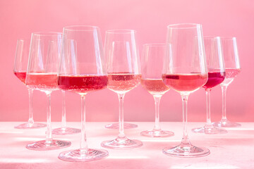 Rose wine, a variety of hues and tints, side view on a pink background, many wineglasses, vibrant summer party