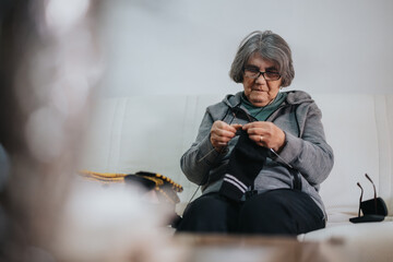 An elderly woman is deeply engaged in knitting, creating a black fabric piece. She sits comfortably...