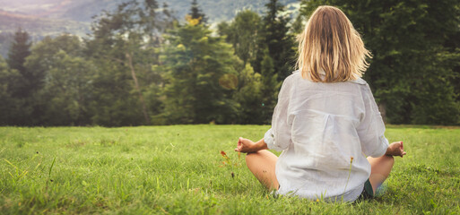Young woman meditating in the meadow in the mountains. View from back.