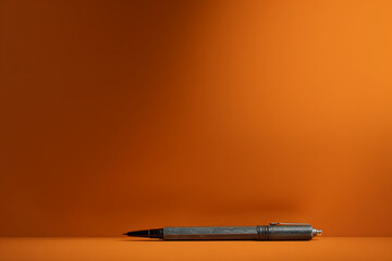 A stylish black pen placed horizontally on a bright orange background