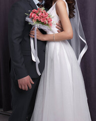 The bride and groom in a white dress hug with a bouquet of flowers