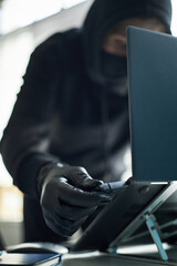 Unrecognizable man wearing black gloves and hoodie inserting USB flash drive with malware into...