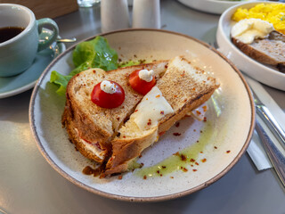 Close-up of an appetizing grilled cheese sandwich, decorated with cherry tomatoes and cream cheese, served with olive oil and chili flakes for a savory meal.