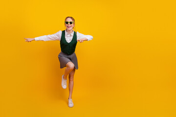 A cheerful student posing joyfully against a vivid yellow background wearing a trendy outfit for...