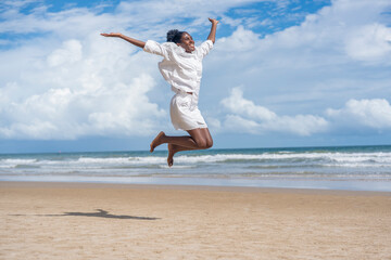 Obraz premium A young carefree woman jumping on sand beach,african female enjoying a summer vacation day in sea shore