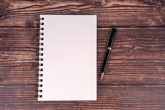 Top view of blank notepad and pen on wooden desk