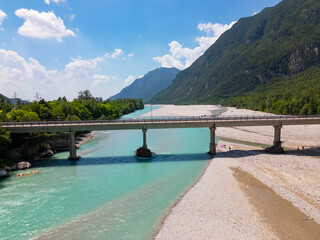 A wide concrete bridge spans the striking turquoise waters of the Tagliamento River near Pioverno, set in an alpine valley with lush greenery