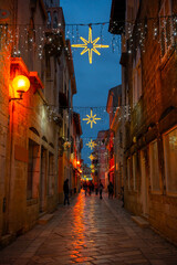 Fototapeta premium Beautiful Christmas decorations with star-shaped lights and glowing garlands adorn a cobbled pedestrian street in Poreč’s historic center