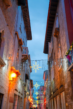 Fototapeta The street of the old town of Poreč at Christmas time. Glowing star and string lights span across a narrow alley framed by old stone buildings