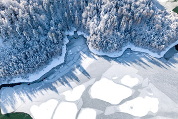 Aerial view of a winding frozen lake flanked by a dense, snow-covered forest. Aesthetic winter...