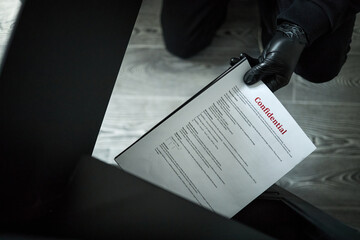 Hands of anonymous man wearing black gloves kneeling on floor, stealing confidential document from...