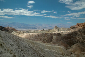 Vibrant multicolored hills and distant mountains in Death Valley under a clear sky, showcasing the dramatic geology of the desert landscape. A natural wonder shaped by erosion and time
