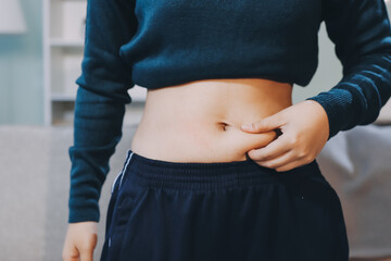Naklejka premium woman's hand holding excessive belly fat, overweight concept