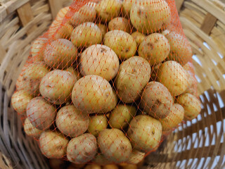 a pile of small, round potatoes in a red mesh bag in the bamboo wicker basket 