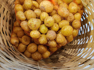 a pile of small, round potatoes in a red mesh bag in the bamboo wicker basket 