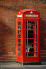 Obraz premium Classic red British telephone booth stands against a weathered brick wall in central London, capturing a timeless symbol of the city's urban identity. A nostalgic urban scene.