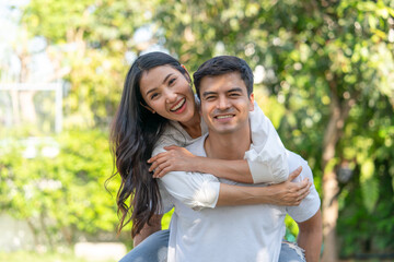 Smiling couple having fun in garden at home while woman playfully rides piggyback on her husband in casual clothes