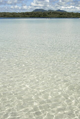 Shallow clear water with distant mountains on a sunny day in Mauritius. A peaceful tropical scene with crystal-clear turquoise water reflecting bright sunlight and calm waves.