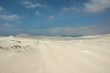 Vast white sand dunes stretch under a partly cloudy sky on the island of Boavista, Cape Verde, near the Atlantic Ocean. A tranquil and expansive desert island view.
