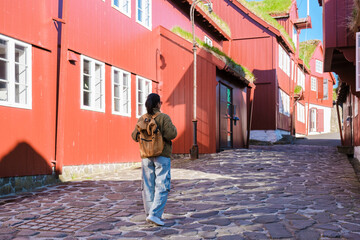 Strolling through an enchanting village in the Faroe Islands, a traveler admires the striking red...