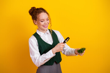 Young red-haired woman studying a plant under a magnifying glass against a vibrant yellow background