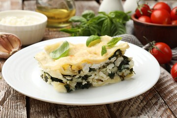 Piece of tasty vegetarian lasagna and ingredients on wooden table, closeup