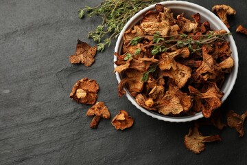 Dried chanterelle mushrooms with thyme on black table, flat lay. Space for text