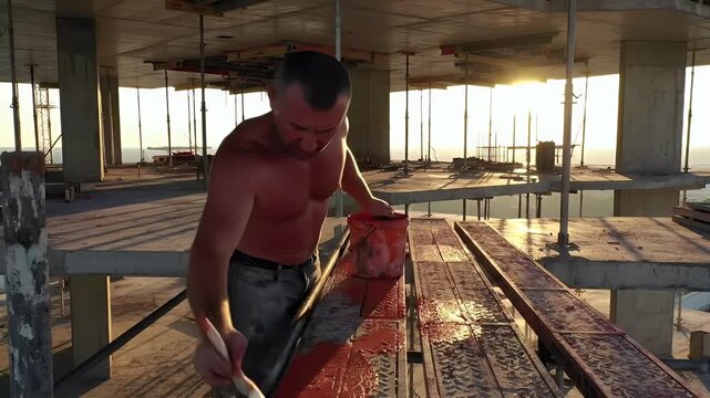 Construction worker applying a protective coating to formwork on a high-rise building site at sunset, symbolizing diligent effort and development.