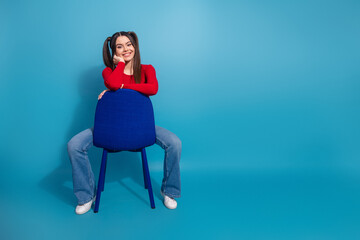 Young woman in stylish outfit sitting on a chair in front of a vibrant blue background showcasing...