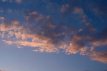 A tranquil evening sky featuring soft clouds illuminated by the warm hues of a setting sun.