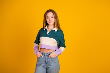 Cute female wearing casual sweatshirt and jeans posing confidently against a vibrant yellow...