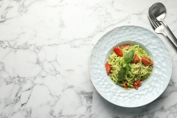 Tasty zucchini noodles with tomatoes, pine nuts and basil served on white marble table, top view. Space for text