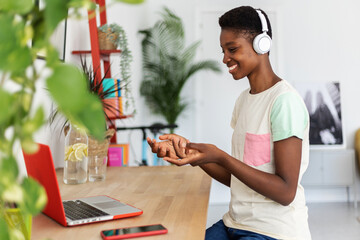 Young happy African woman working or studying on laptop from home office talking with someone...
