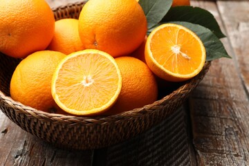 Fresh oranges and leaves in wicker basket on wooden table, closeup