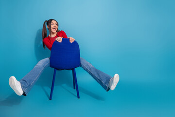 Excited young woman sitting energetically with playful expression against vibrant blue backdrop in...