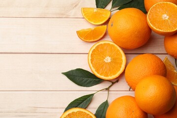 Fresh ripe oranges and leaves on light wooden table, flat lay. Space for text