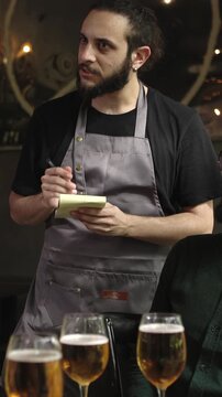 Vertical HD video of young waitress writing on notepad taking order from group of friends at restaurant