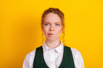 Thoughtful young student with red hair and green waistcoat on yellow studio background reflecting...