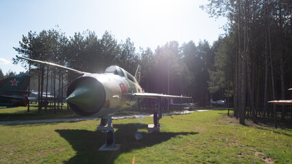 A vintage Soviet jet on display in an aircraft museum, surrounded by lush trees and warm sunshine, highlights the beauty of historical aviation.