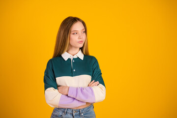 Stylish young girl in a casual sweatshirt stands with crossed arms against a vibrant yellow...