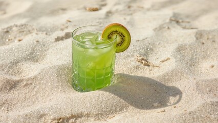 Kiwi cocktail in a clear glass with ice garnished with a slice of kiwi on sandy beach surface under daylight conditions